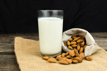 Milk with almond or roasted almond on sack with a wooden table on dark background. Healthy food. Snack. Food and drink concept.