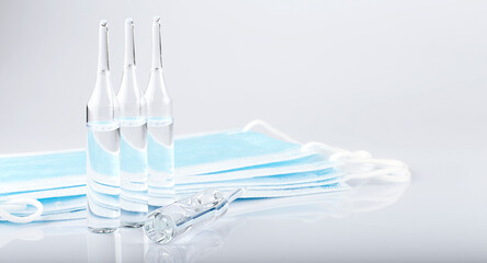glass ampoules and a syringe with medical protective masks on white background, global vaccination concept