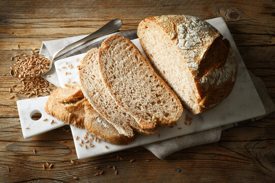 Sliced organic spelled bread on old wooden table with seeds, marble cutting board and tea towel.
