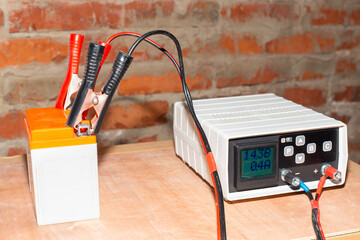 Charging the motorcycle battery. On a wooden surface against the background of a brick wall of the...