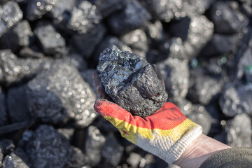 Extraction of mineral resources of hard coal. A man holds in his hand a large piece of coal,...