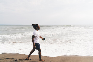 Black man in earphones walking on beach