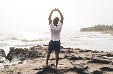 Anonymous man with arms raised on beach