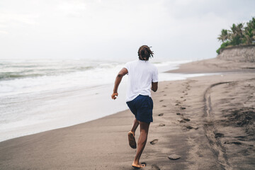 Unrecognizable ethnic man running on empty seashore