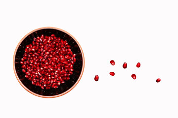 Pomegranate seeds in black bowl on white background.