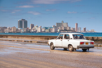 Famous skyline of Havana and its hotels in the Vedado district, seen from the Malecon, while an old Soviet-era car speeds by.