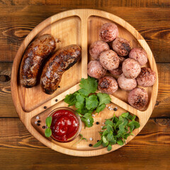 Fried sausages and meat balls with sauce and herbs on a wooden plate. Top.