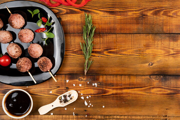 Meat balls on wooden skewers lie on a black plate. Sauce, spices,  rosemary.