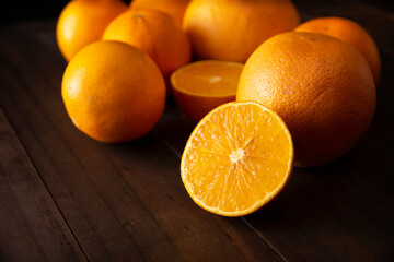 close up of a ripe orange cut in half and several whole oranges on brown rustic wooden table with copy space