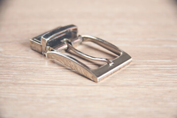 Square nickel plated buckle with flat tongue on a wooden background.