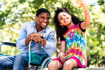 Man in a wheelchair taking a selfie with her daughter.