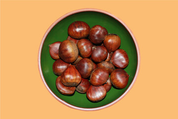 Chestnuts in green bowl against orange background.