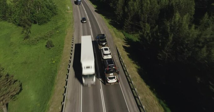 Auto transporter Semi Truck driving, traveling alone on asphalt straight road in dense flat forest , highway top view follow vehicle aerial footage. Freeway trucks traffic
