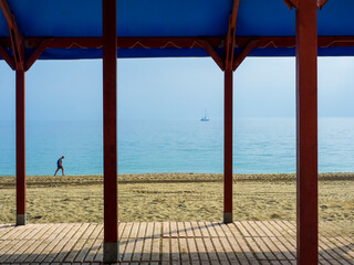 Vista desde una pergola de madera de una persona paseando por la orilla de la playa