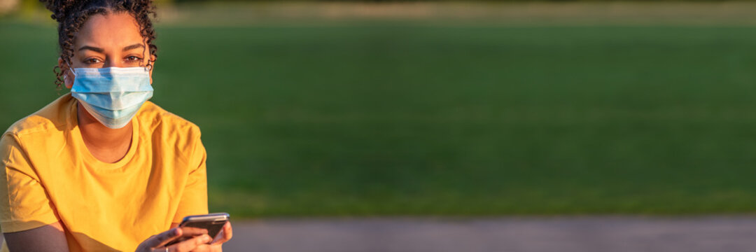 African American Teenager Girl Woman Wearing Coronavirus COVID-19 Face Mask and using a mobile cell phone - Powered by Adobe