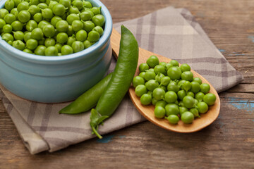 Green peas in blue bowl, green pods and wooden spoon on table