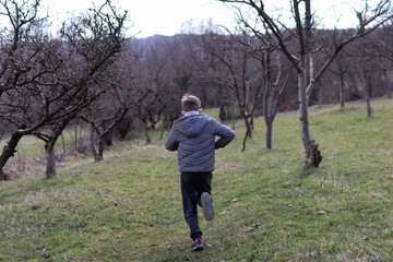 Naklejka na ściany i meble Young boy running across a meadow through an alley in nature on an early spring day in the countryside