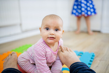 Adorable baby sitting between the feet of her father