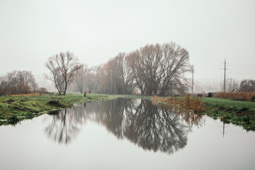 Fisherman catches fish early in the morning. Landscape pier moody rainy weather day outside, dark clouds nature trees water flow, rum on green grass, wetlands swamp dirty. Image with copy space. 
