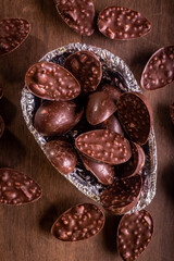 Top view of a close up of mini stuffed chocolate easter eggs inside of a half of an easter egg wrapped in an aluminium paper. Some mini stuffed easter eggs around it on a wooden table.