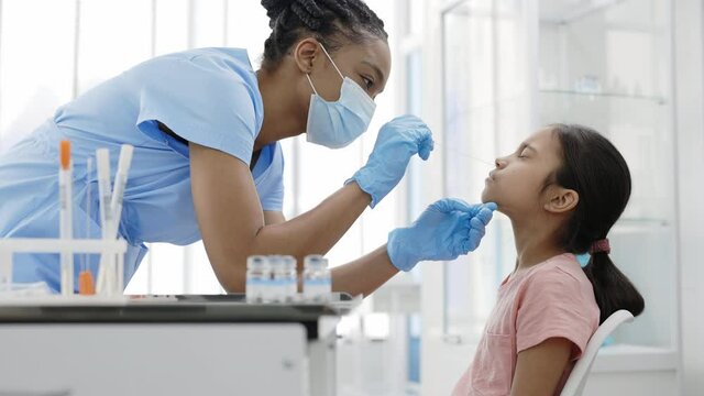 Crop view of medical female nurse in protectivemask and gloves taking swab from nose of little girl in hospital. Concept of PCR diagnostic method, rapid covid test.