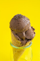 Chocolate ice cream in a waffle cone on the yellow  background. Location vertical. Close-up.