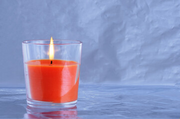 Aroma candle orange close-up in a glass on metallic gray background.