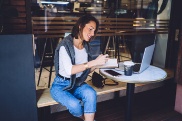 Cheerful woman writing notes in cafe