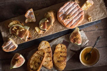 Crostini on a wood backghround with camembert ,figs ,honey  and rosemary .
Cheese delisious board 