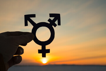 Transgender symbol in the hand of a man against the background of the sunset.