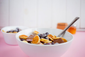 Pancake cereal in a plate with blueberries and chocolate on a pink table.Trendy modern breakfast with little pancakes.