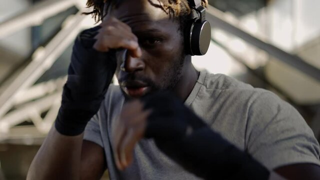 Afro american young male boxer practicing shadow boxing around the metal structures, close up