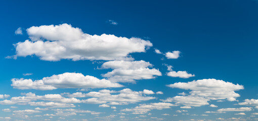 Group of idyllic floating white clouds on azure blue sky background. Tranquil natural panoramic cloudscape scene with copy space in top right corner. Environment or ecosystem, weather and meteorology.