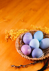 Easter pastel colored eggs in a wicker basket on a wooden table with copy space