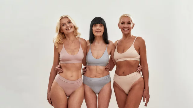 Looking Great Over 50. Three attractive middle aged women in underwear  embracing each other while posing together on light background Stock-bilde