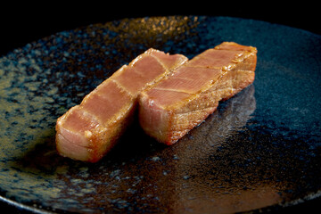 Fresh tuna steak served on a black plate. Isolated on a black background. Seafood