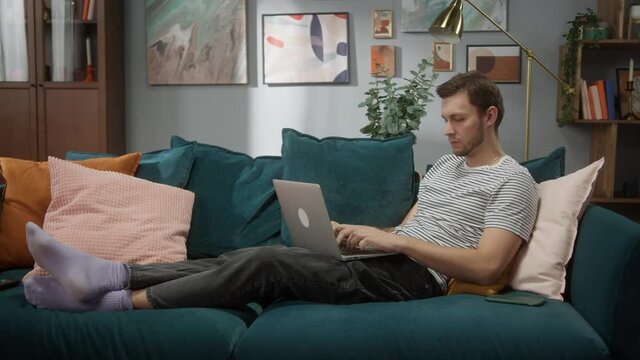 Portrait of tired man sitting at sofa and working remote on computer desktop in cozy room at day, Work hard and too concetration, home freelance, coding new programm, daylight, professional employee 