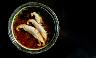 Japanese miso soup with onions, seaweed and eryngii mushrooms, served in a black bowl. Isolated on a black background. Diet food