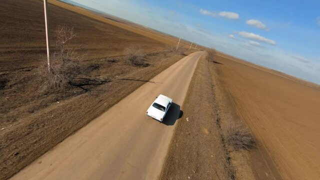 Fpv sport drone with action camera follows Old Soviet Car Volga 24 on the Lonely Road Between Brown Fields. Fpv Racing drone first Person cinematic chase view.