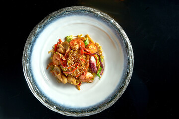 Glass rice noodles in sweet and sour sauce with shrimp, scallops, octopus and squid, served in a white bowl. Wok noodles. Isolated on a black background. Street thai food