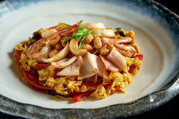 Glass rice noodles in sweet and sour sauce with shrimp, scallops, octopus and squid, served in a white bowl. Wok noodles. Isolated on a black background. Street thai food
