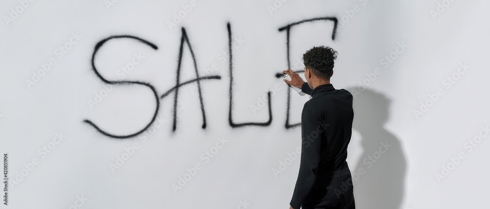 Wall mural rear view of young man writing word sale on wall