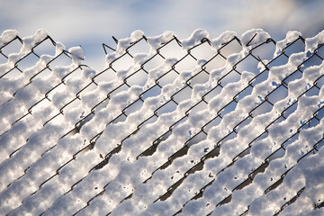 Metal mesh is covered with snow. Winter background