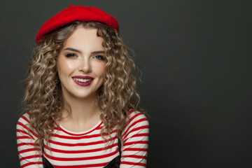 Happy cheerful woman dressed in striped t-shirt and red french style beret smiling on black background