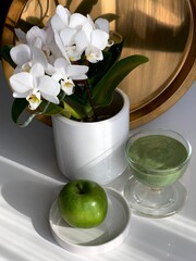 green apple and green smoothies with flowers orchid on a white background as an example of healthy food