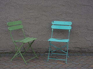 Two chairs in front of a grey wall sitting outside.