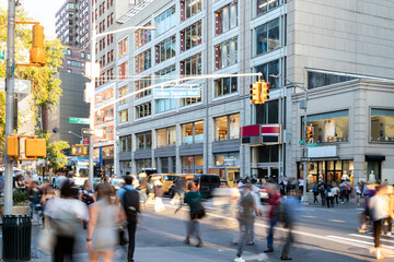 Crowds of people walking across the busy intersection on 14th Street at Union Square Park in New York City past the cars and buildings