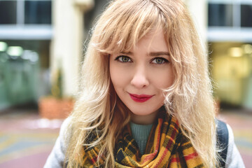 Fototapeta premium Urban portrait of a beautiful smiling Caucasian girl with blond curly hair looking at the camera