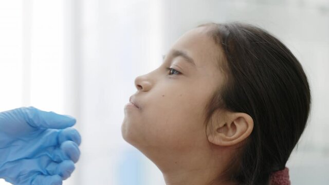 Close up view of medical worker in protective gloves taking swab from nose of little girl. Concept of PCR diagnostic method, rapid covid test.