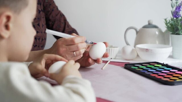Mom and son paint patterns on Easter eggs at home in the kitchen